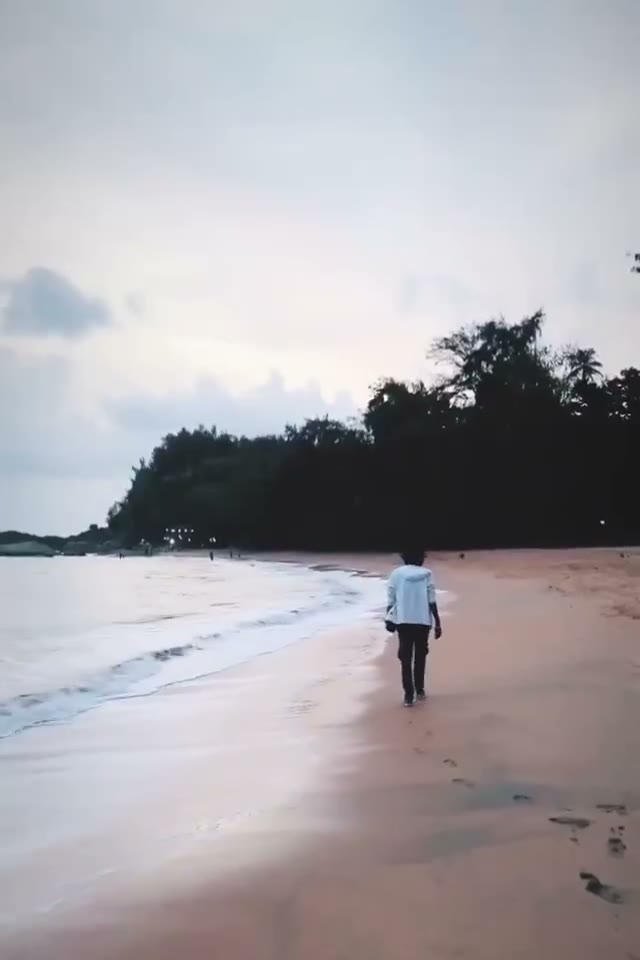 A solo walk along a quiet Kerala beach at dusk, waves rolling in beside the treeline